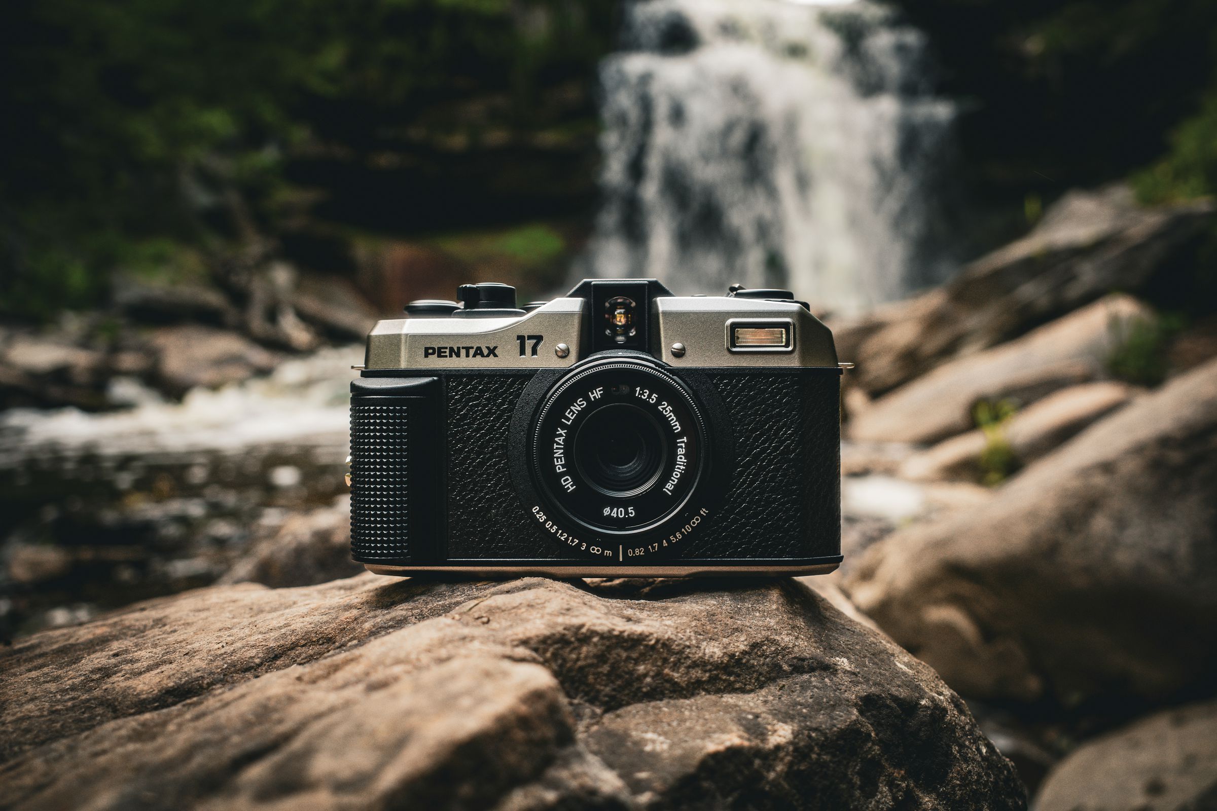 The Pentax 17 film camera resting on rocks in front of a waterfall.