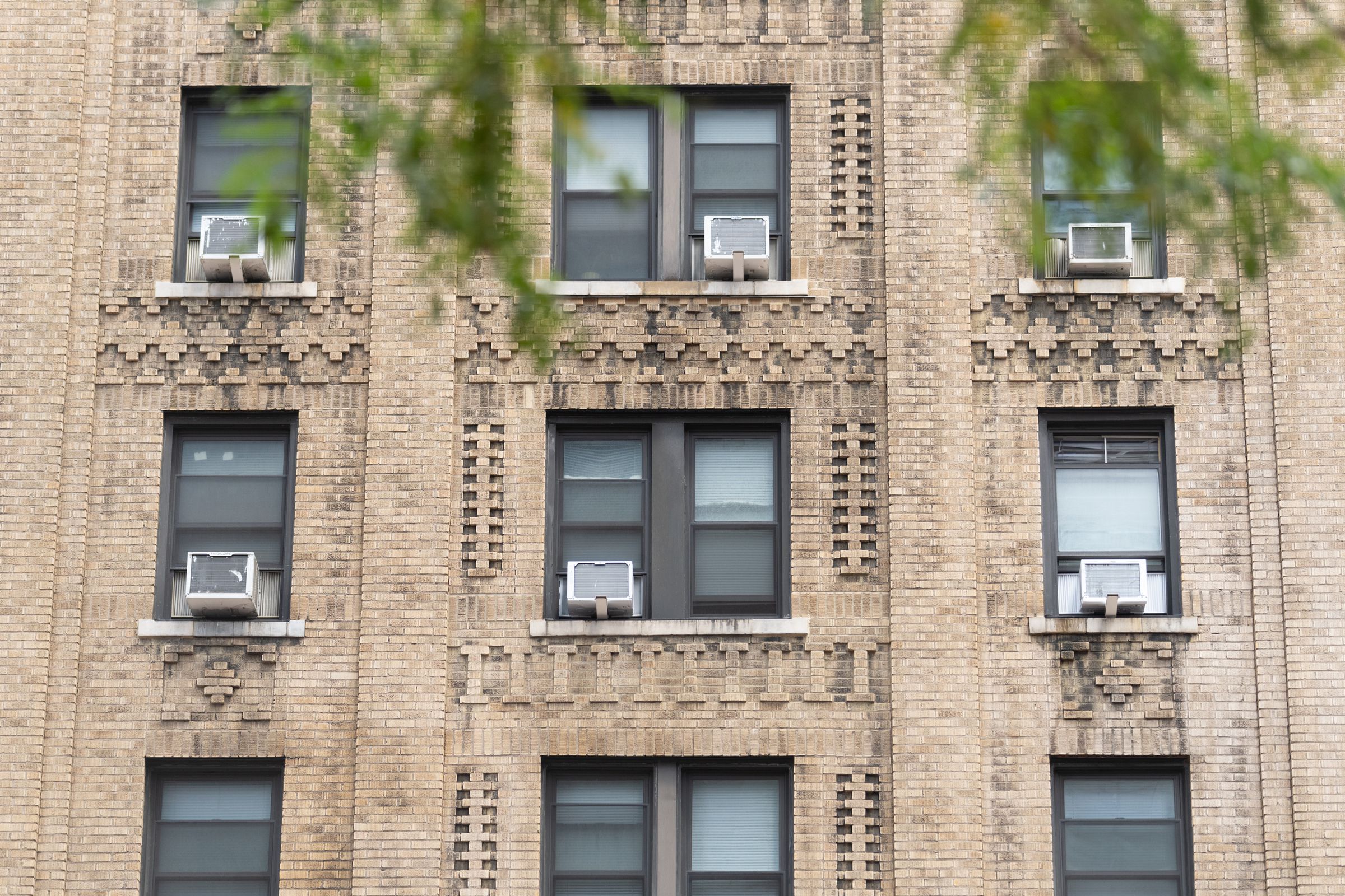 Three rows of windows on the side of an apartment building with air conditioning units jutting out from several windows. 