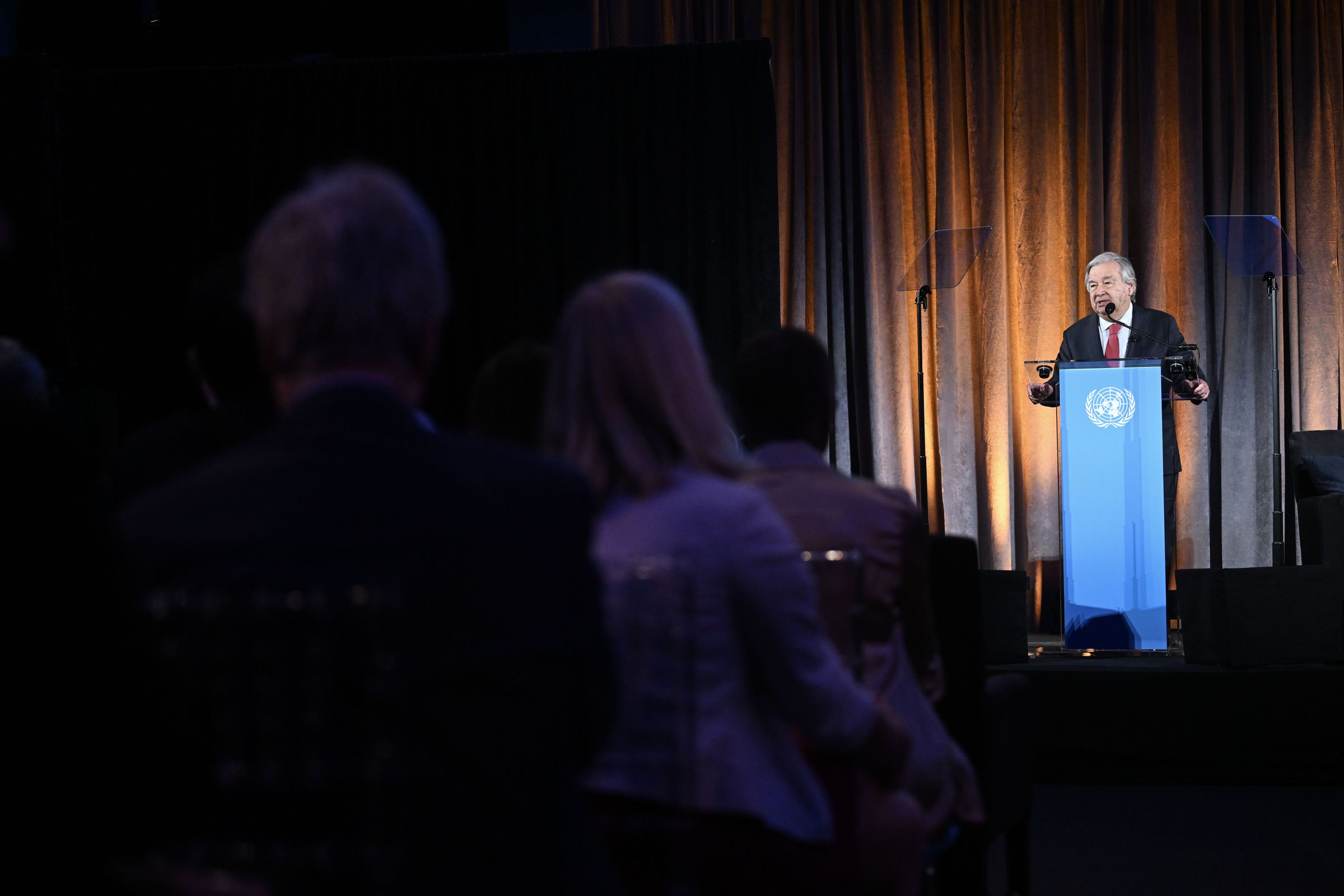 A man in a suit speaks at a podium in front of a crowd.