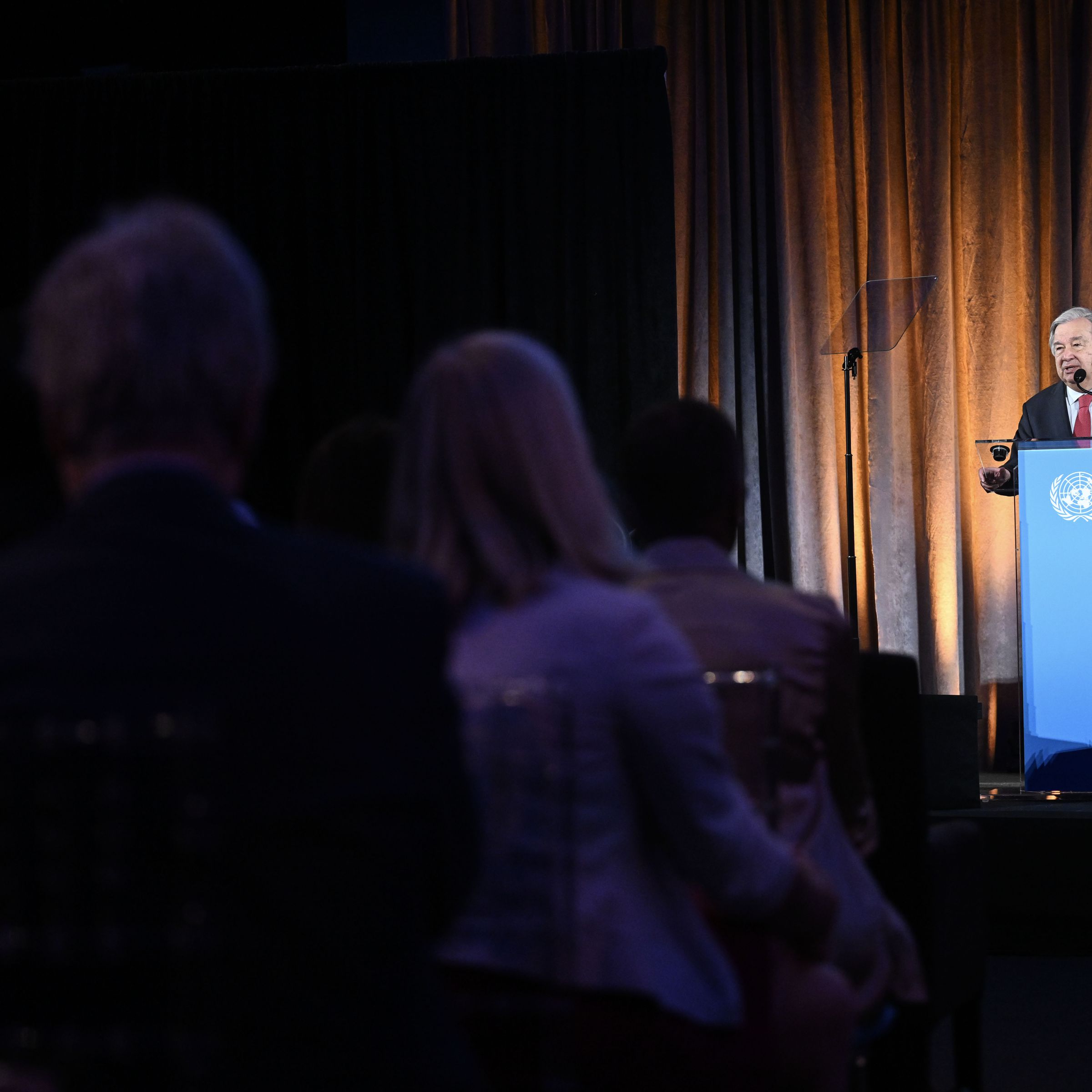 A man in a suit speaks at a podium in front of a crowd.