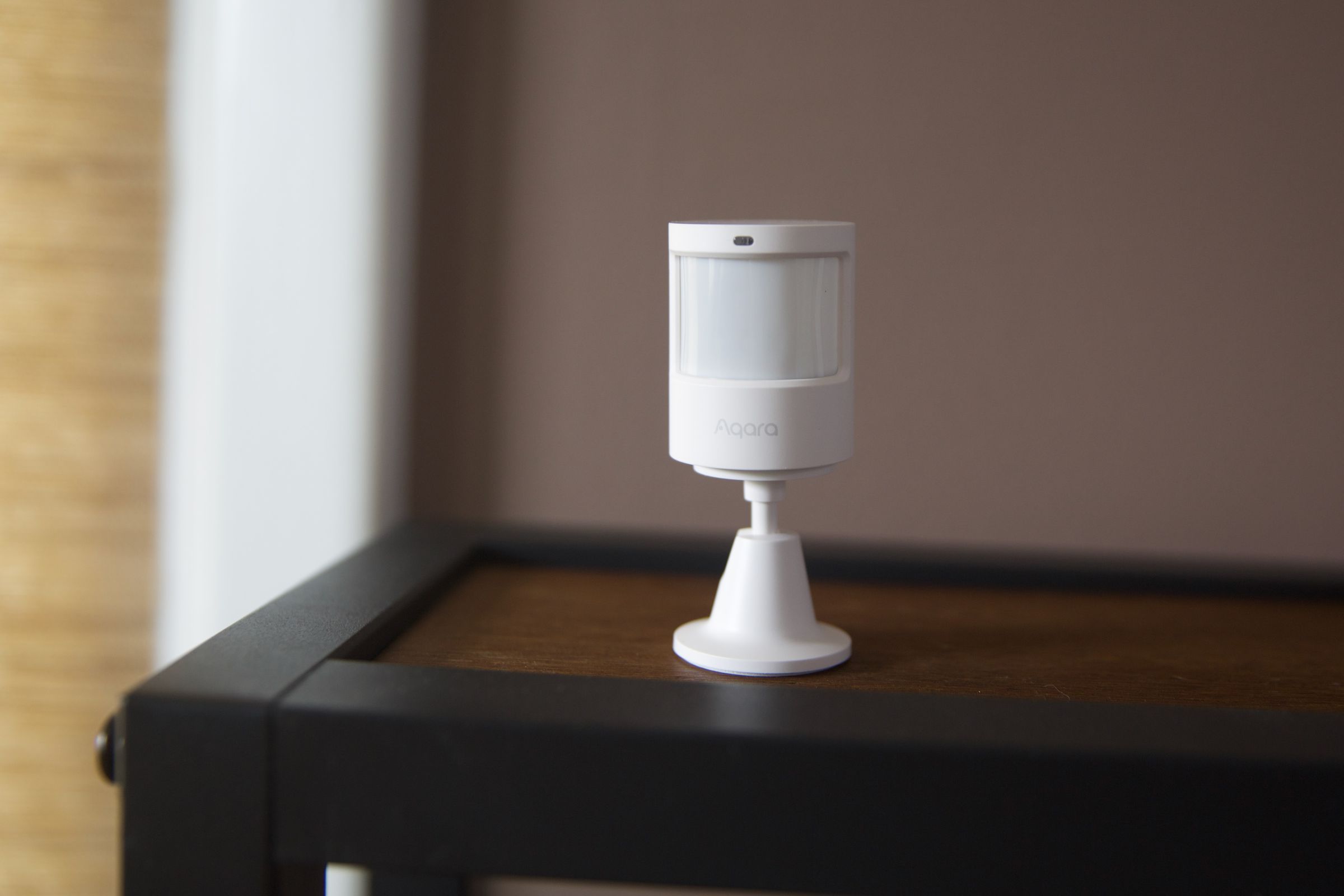 A white motion sensor on a wooden shelf.