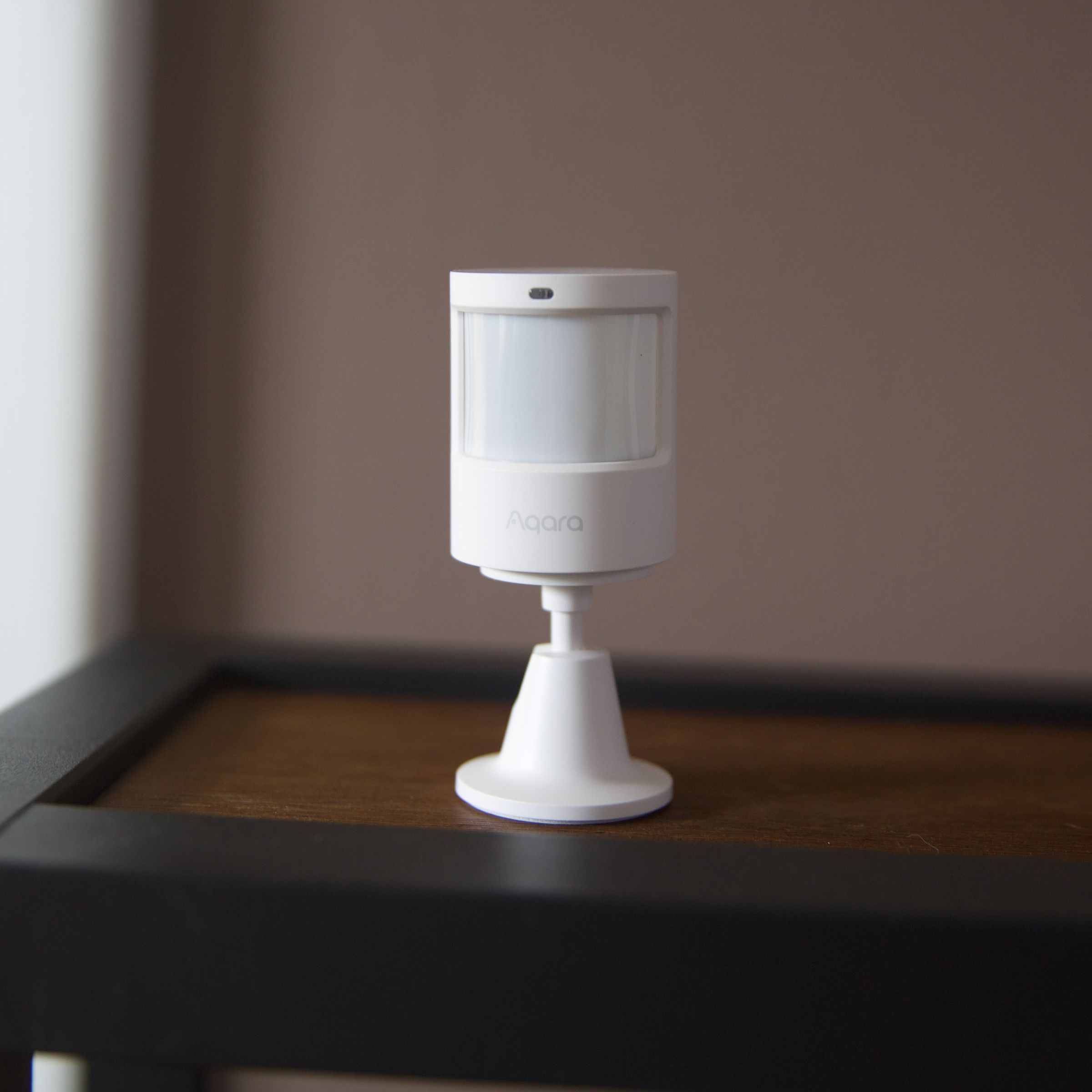 A white motion sensor on a wooden shelf.