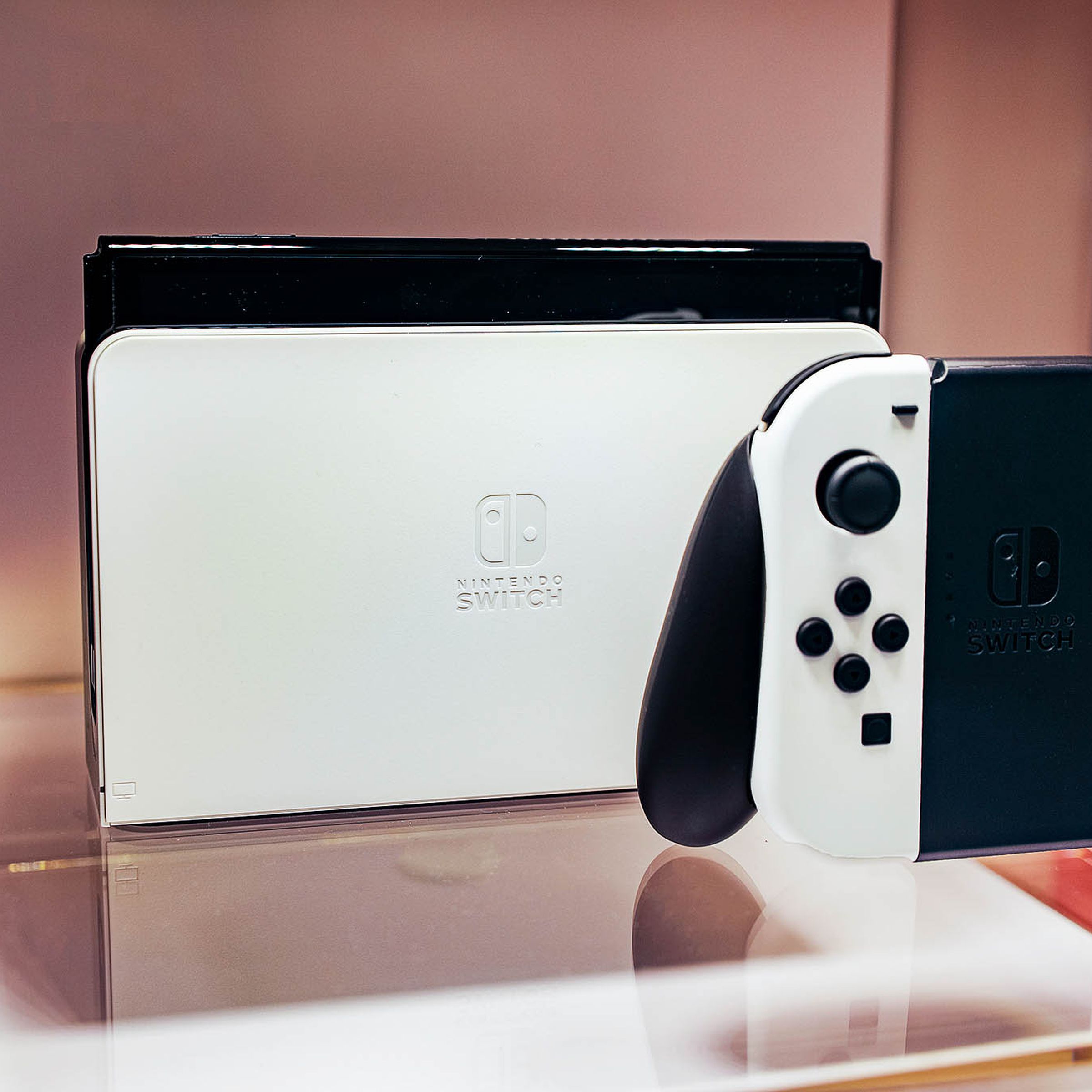 A docked Nintendo Switch OLED model sitting on a piece of glass next to its controller.