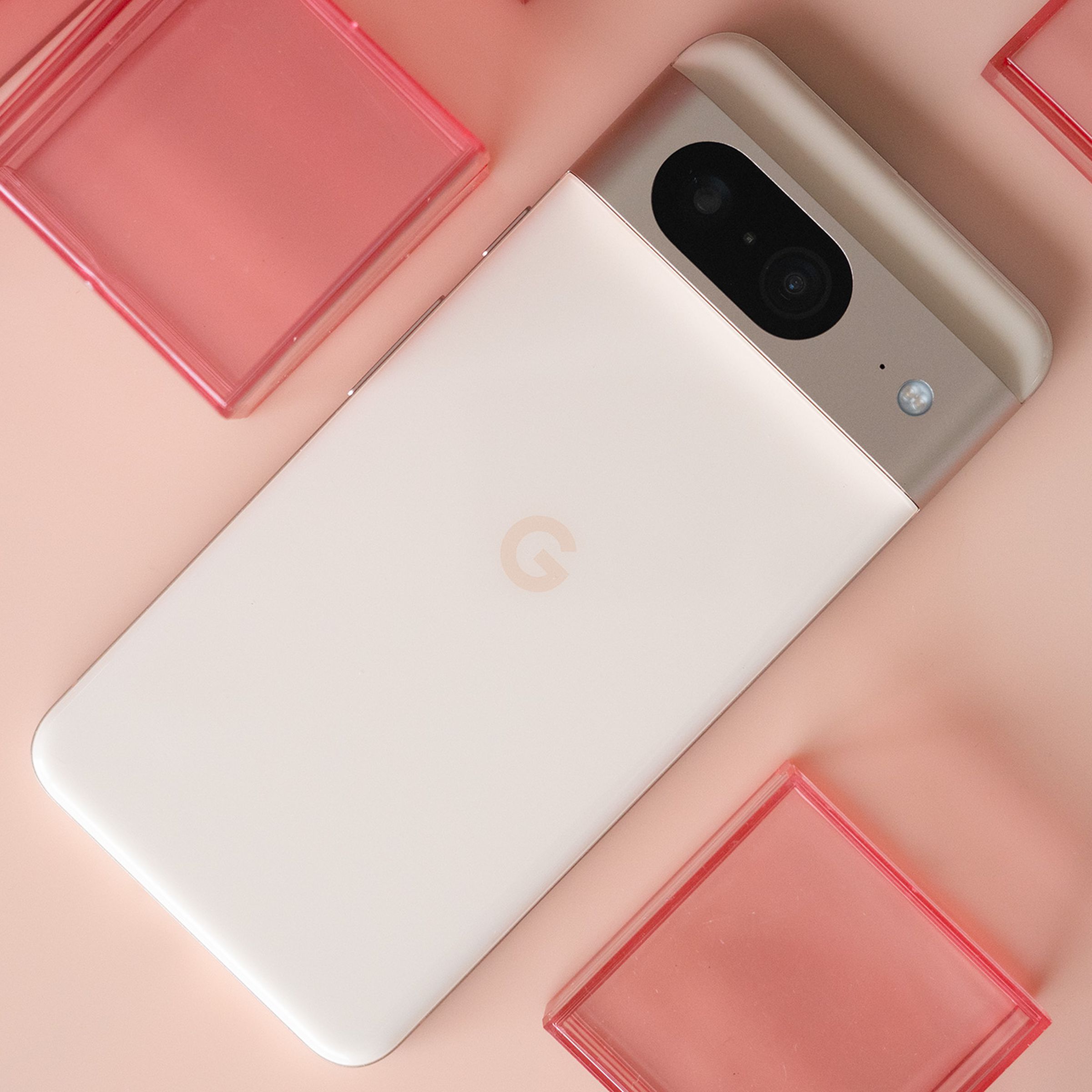 Google Pixel 8 with rear panel facing up in pink on a light pink background with red plastic cubes