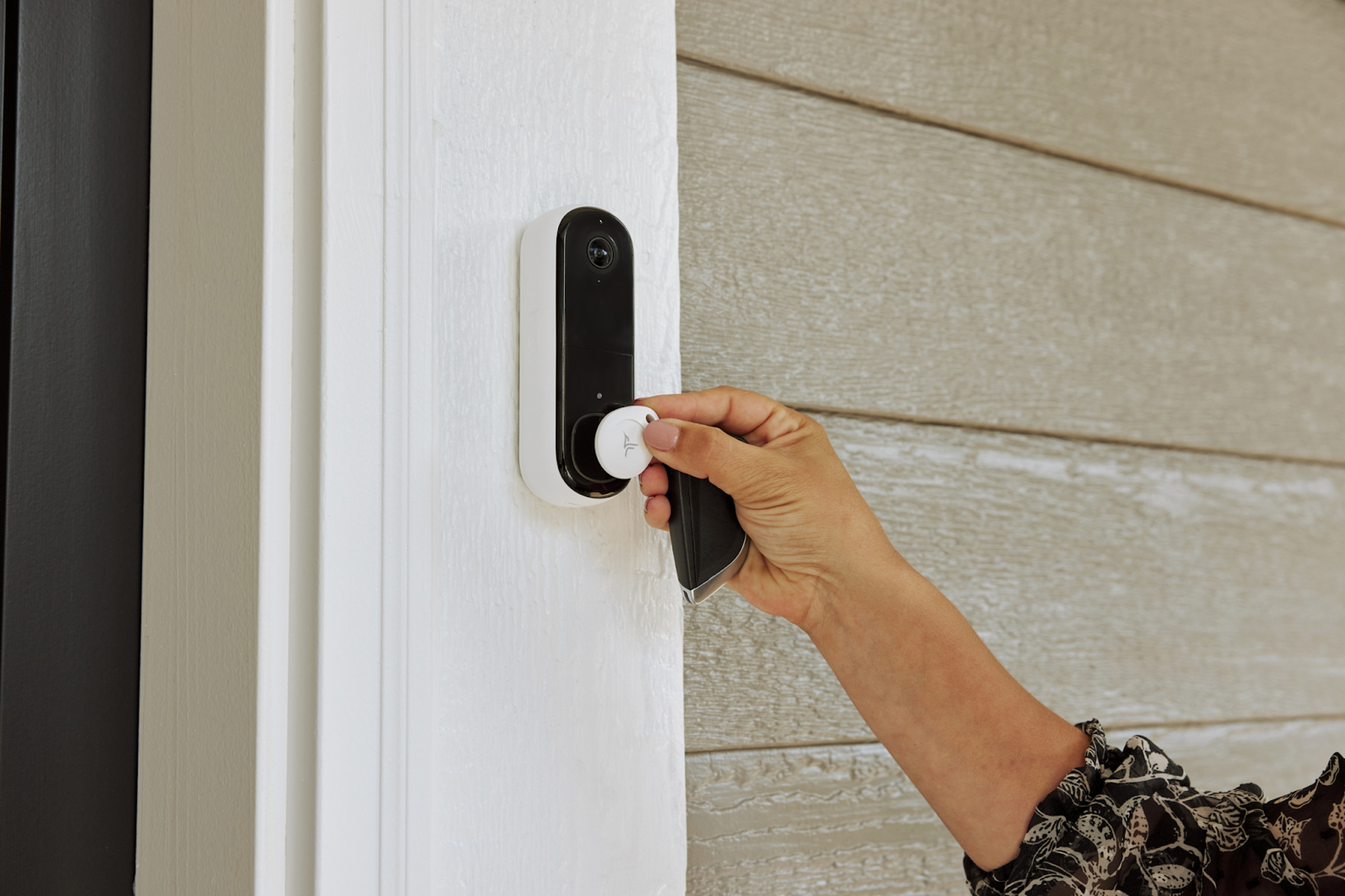 A person holding an Arlo security tag up to a doorbell.