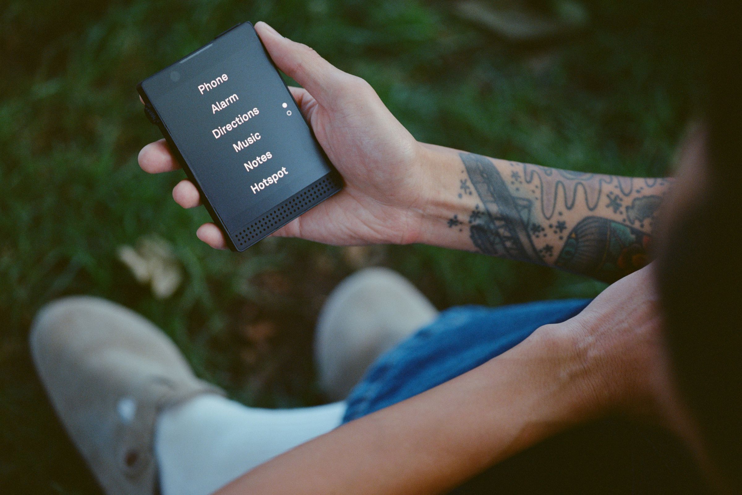 A person holding a Light Phone 3, over grass.