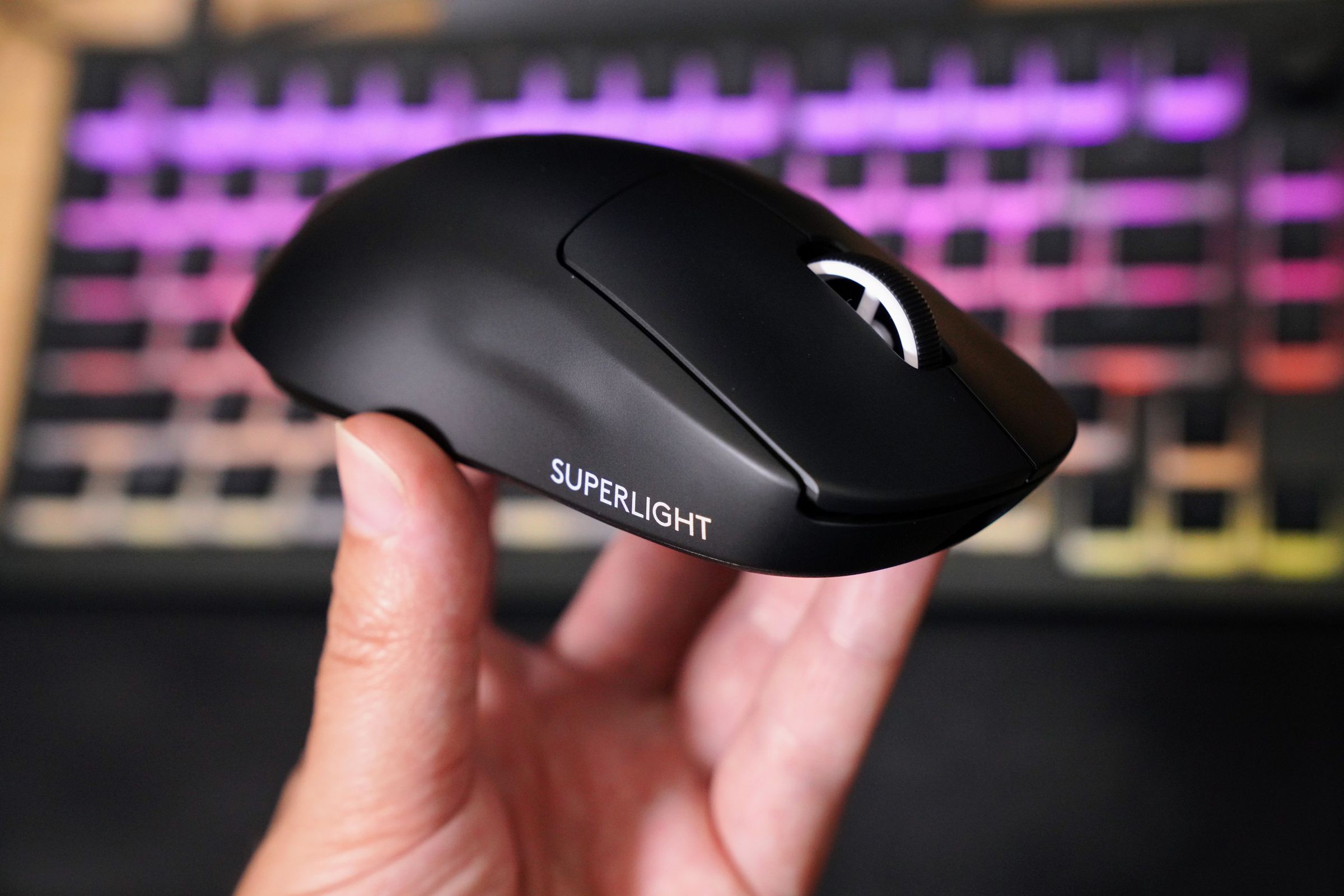 A hand holds up a jet black sculpted plastic mouse with a white scroll wheel and white words “Superlight” printed on the side.